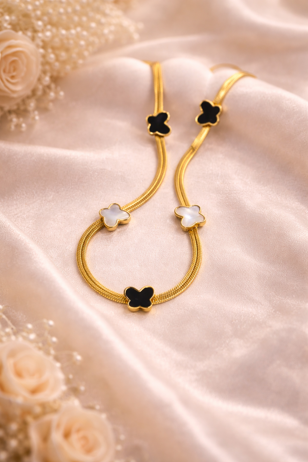 Gold necklace with black and white stones on a soft pink fabric background