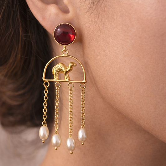 Gold earring with a red gemstone and camel design worn by a person.