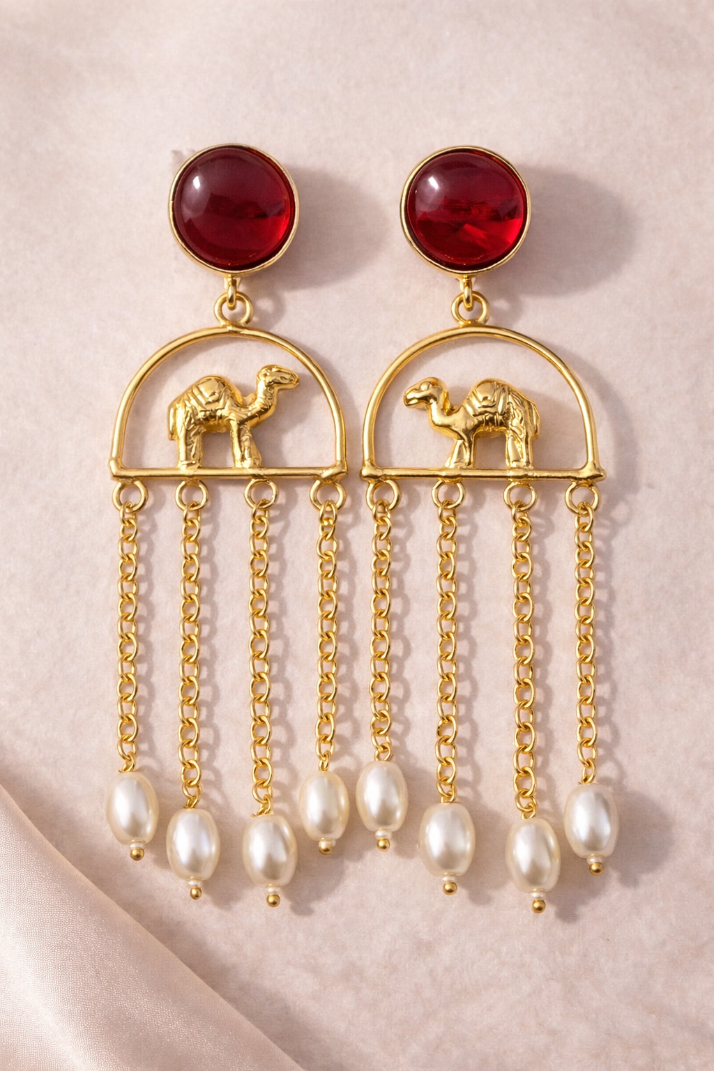 Gold earrings with red gemstones and camel designs on a beige background