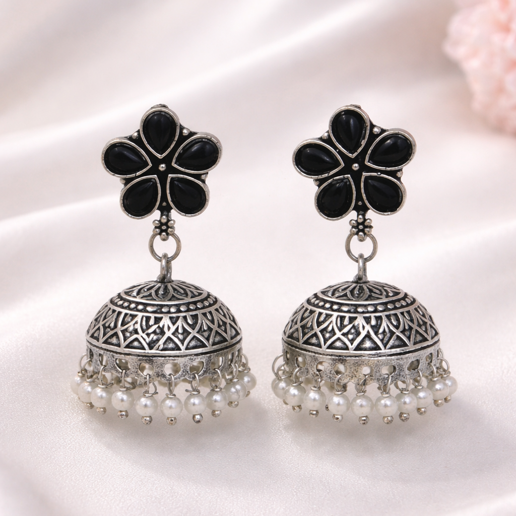 Pair of black and silver earrings with pearl accents on a white fabric background