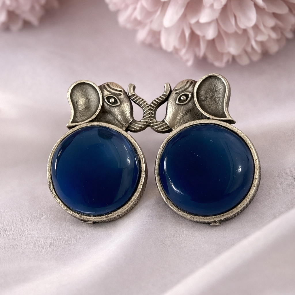 Pair of blue earrings with silver accents on a soft pink fabric background
