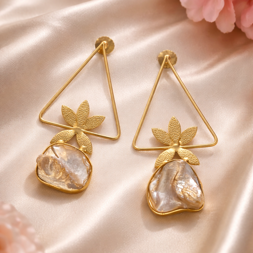 Gold earrings with leaf designs on a pink satin background
