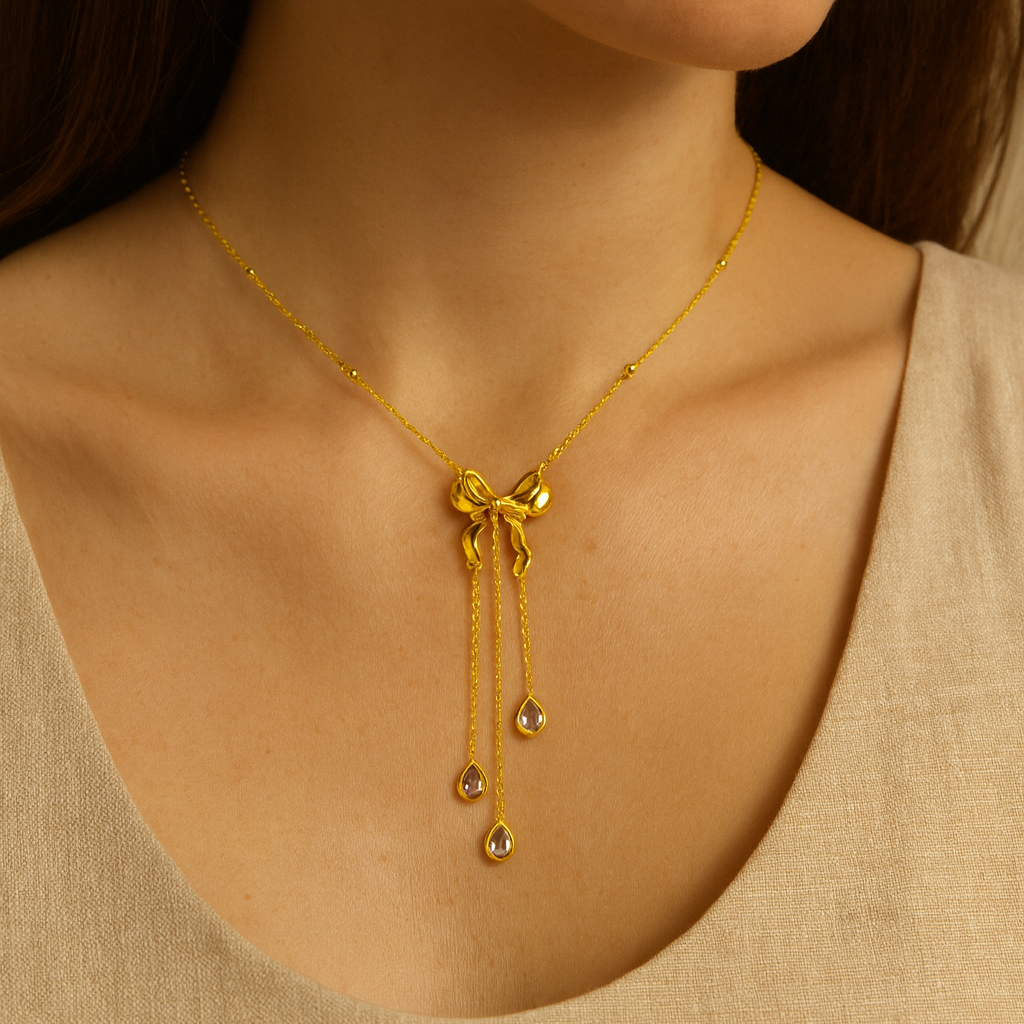 Gold necklace with a bow and dangling elements worn by a person.