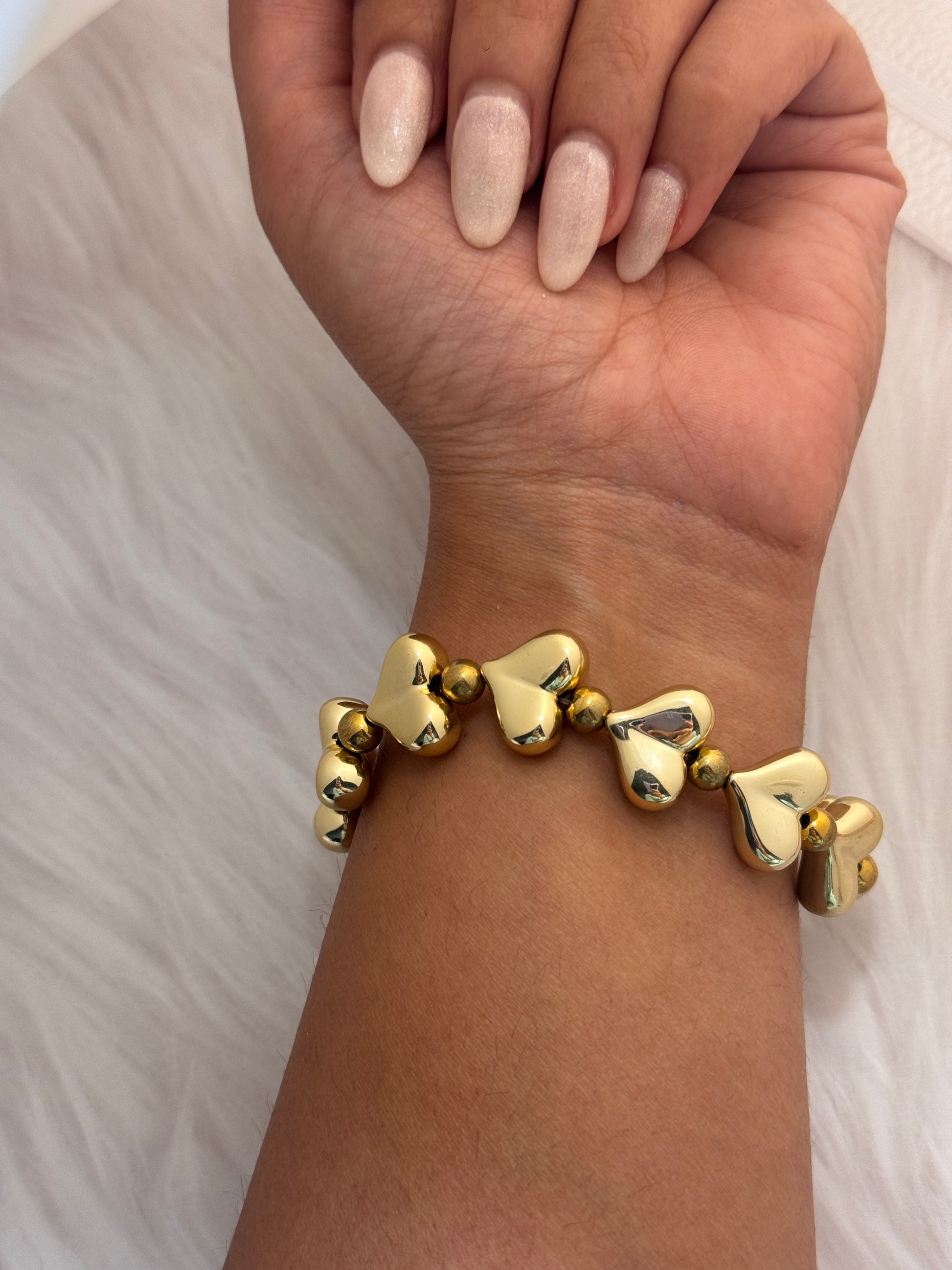 Gold heart-shaped bracelet on a wrist with a neutral background