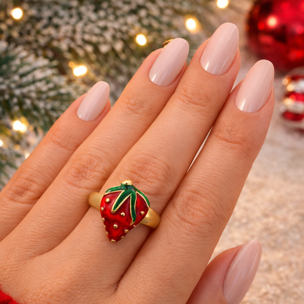 Hand wearing a strawberry-shaped ring with a Christmas tree and decorations in the background