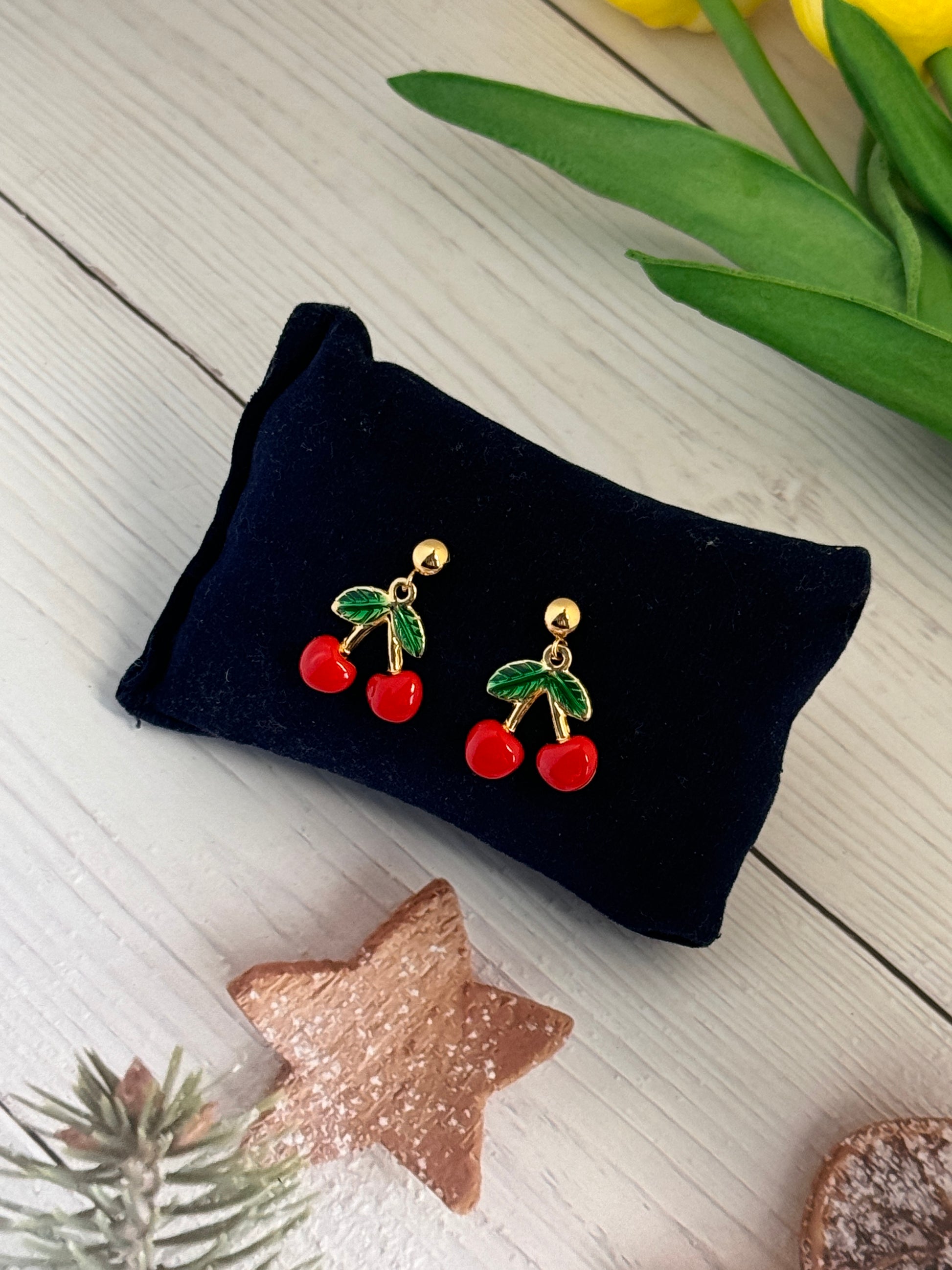 Cherry-themed earrings on a black stand with decorative items around