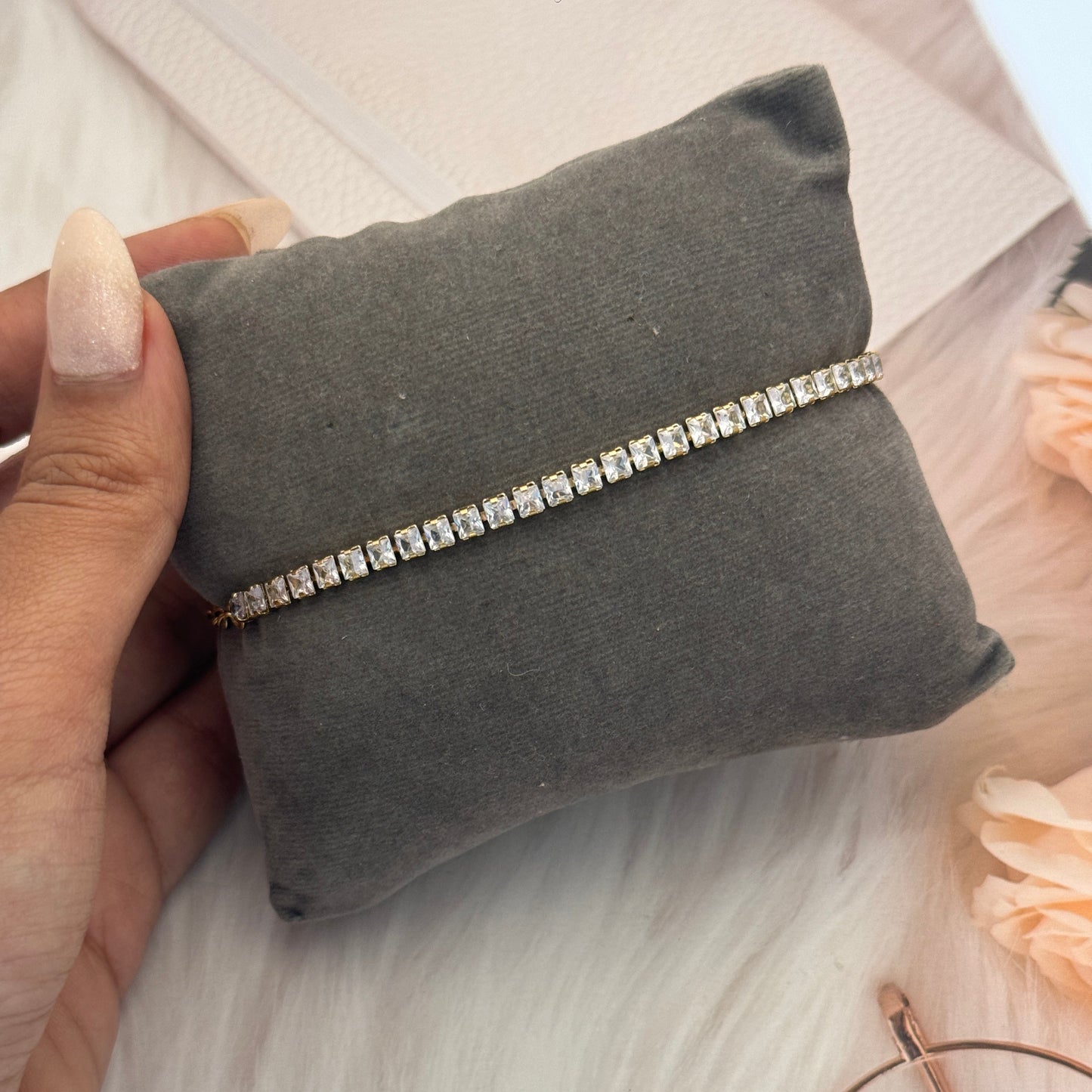 Silver bracelet on a gray cushion held by a hand with a blurred background