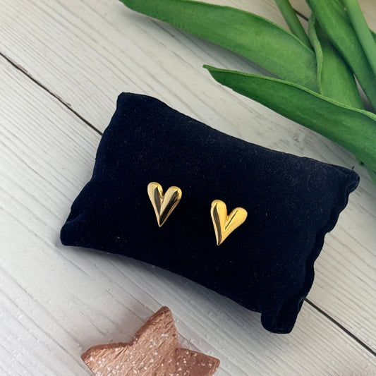 Gold heart-shaped earrings on a black pillow with tulips and a star decoration in the background.