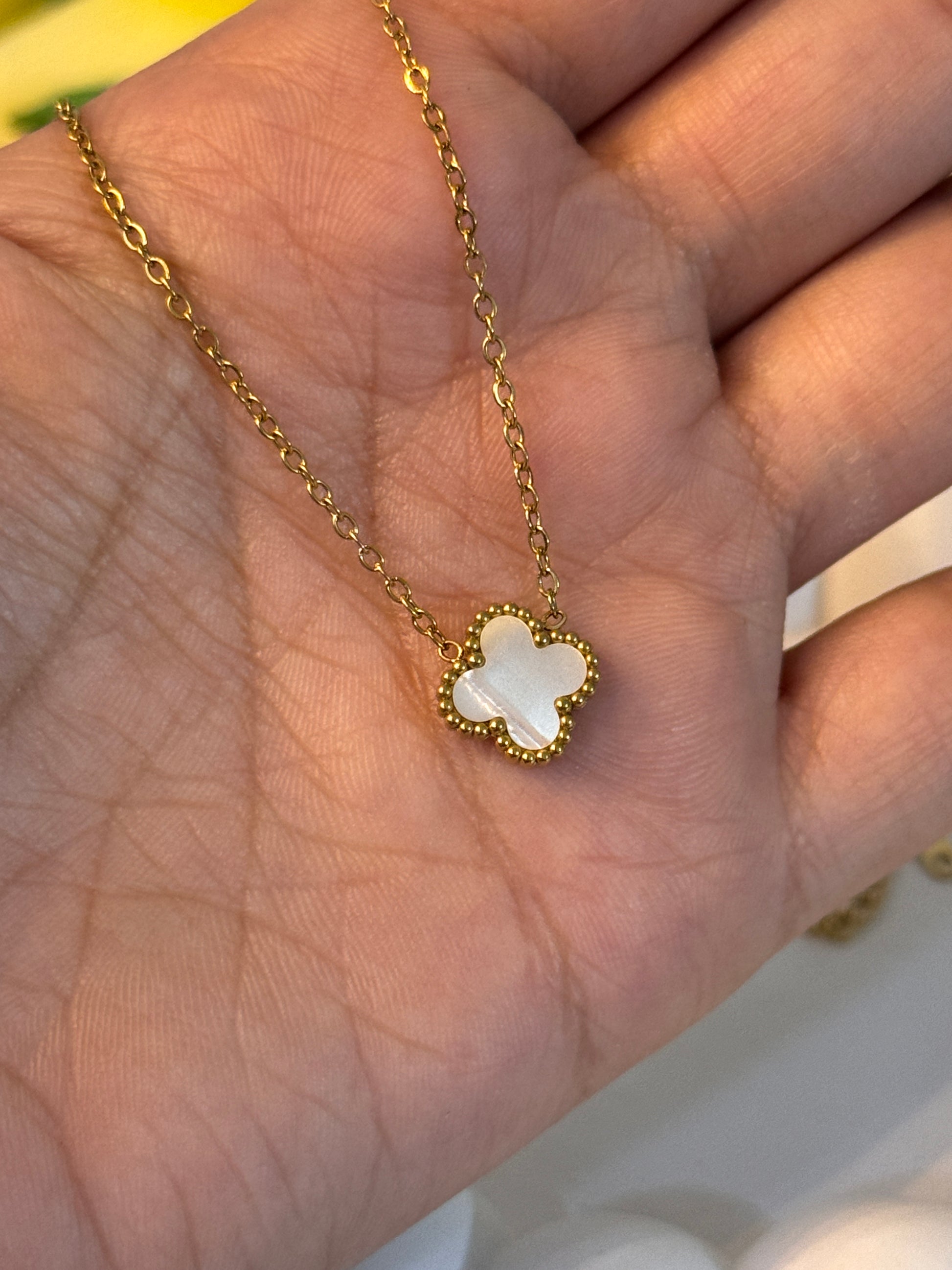Gold necklace with a clover-shaped pendant held in a hand.