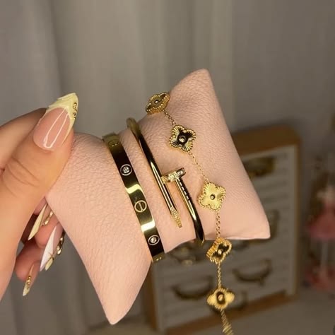 Hand holding gold bracelets on a pink cloth with a blurred background