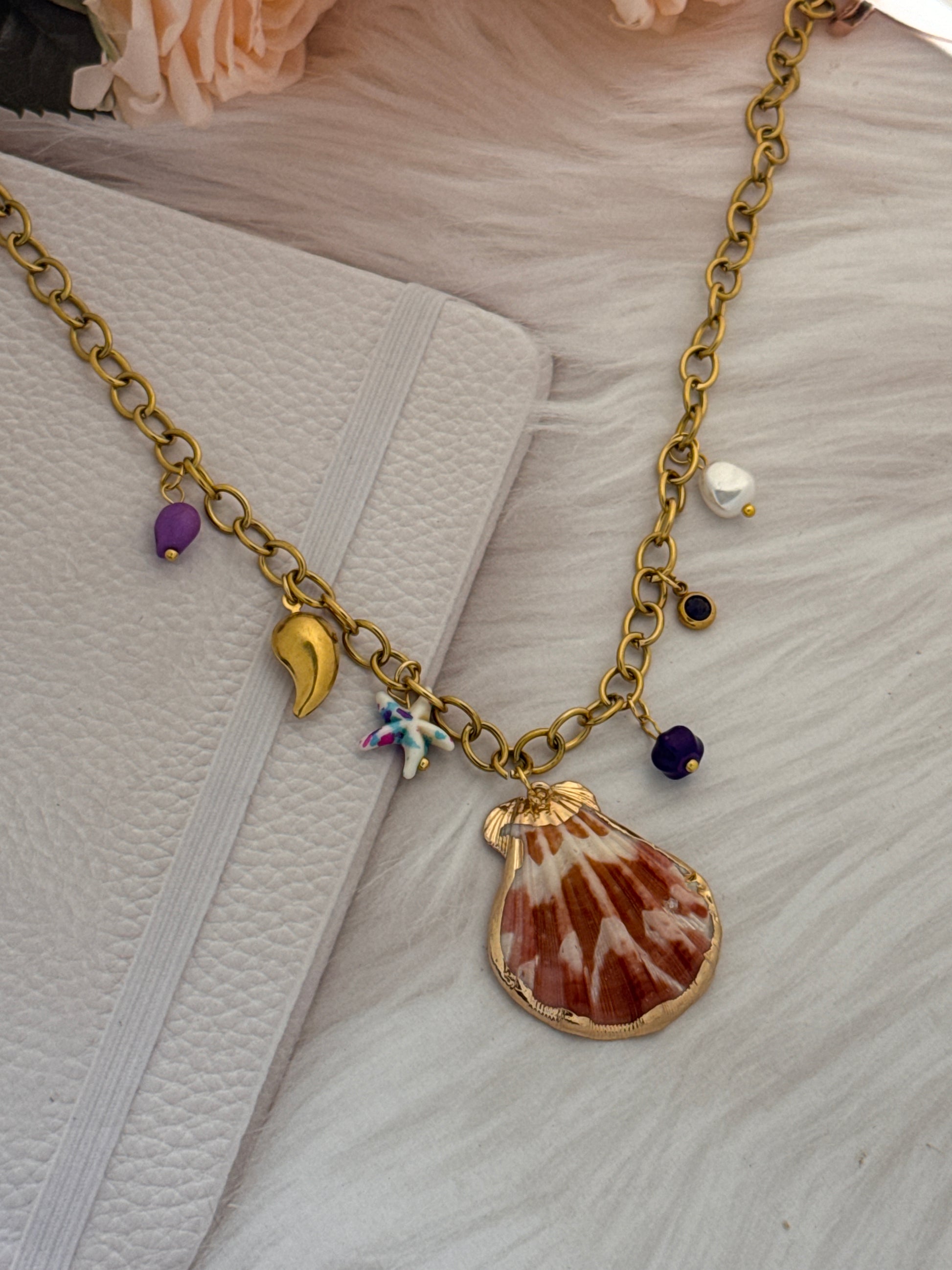 Gold chain with shell and flower charms on a textured surface
