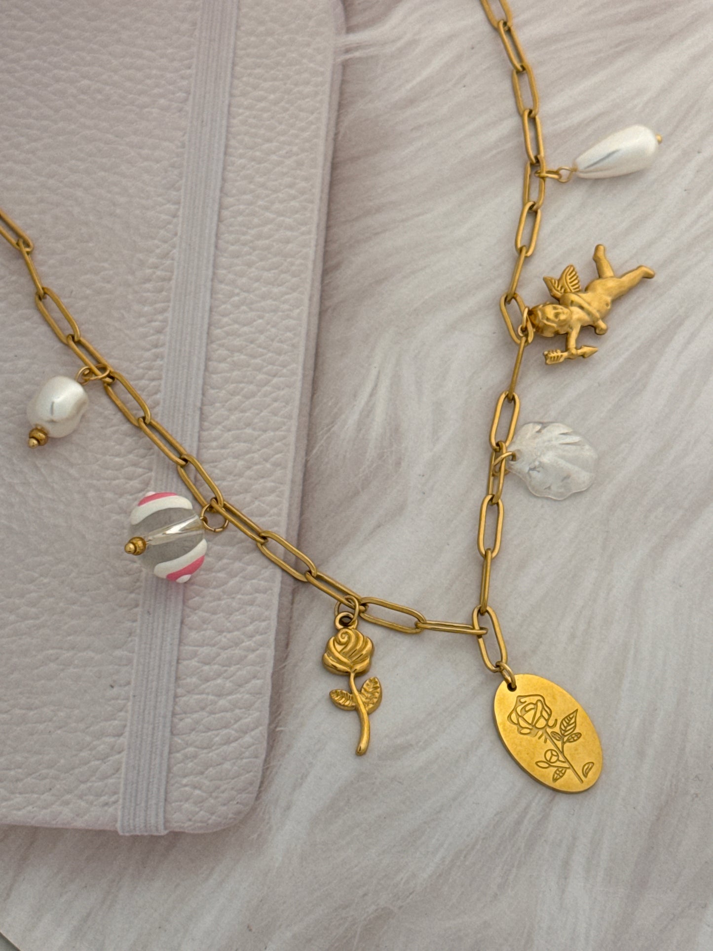 Gold chain necklace with various charms on a textured surface