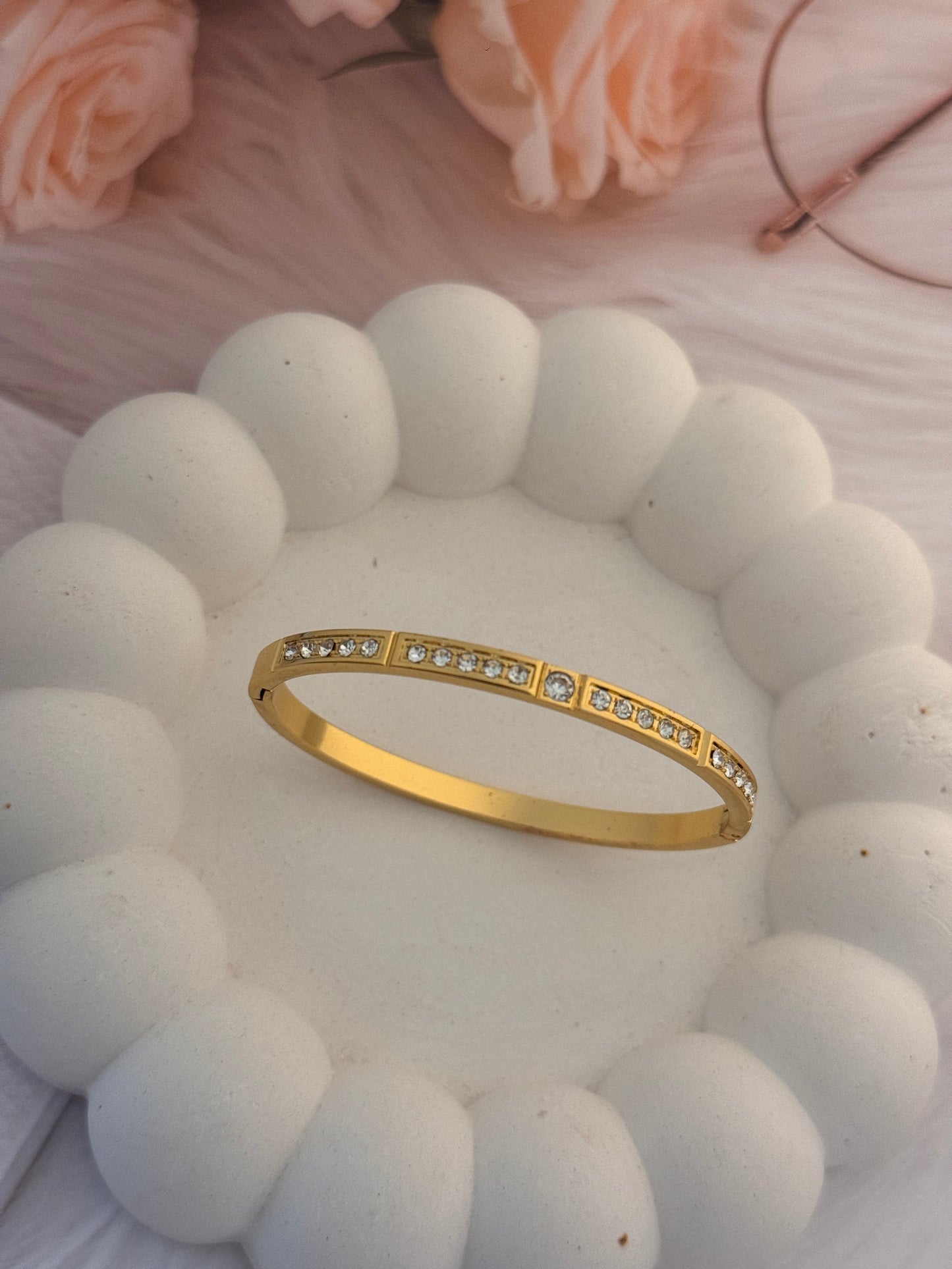 Gold bracelet with small diamonds on a textured white surface with pink roses.