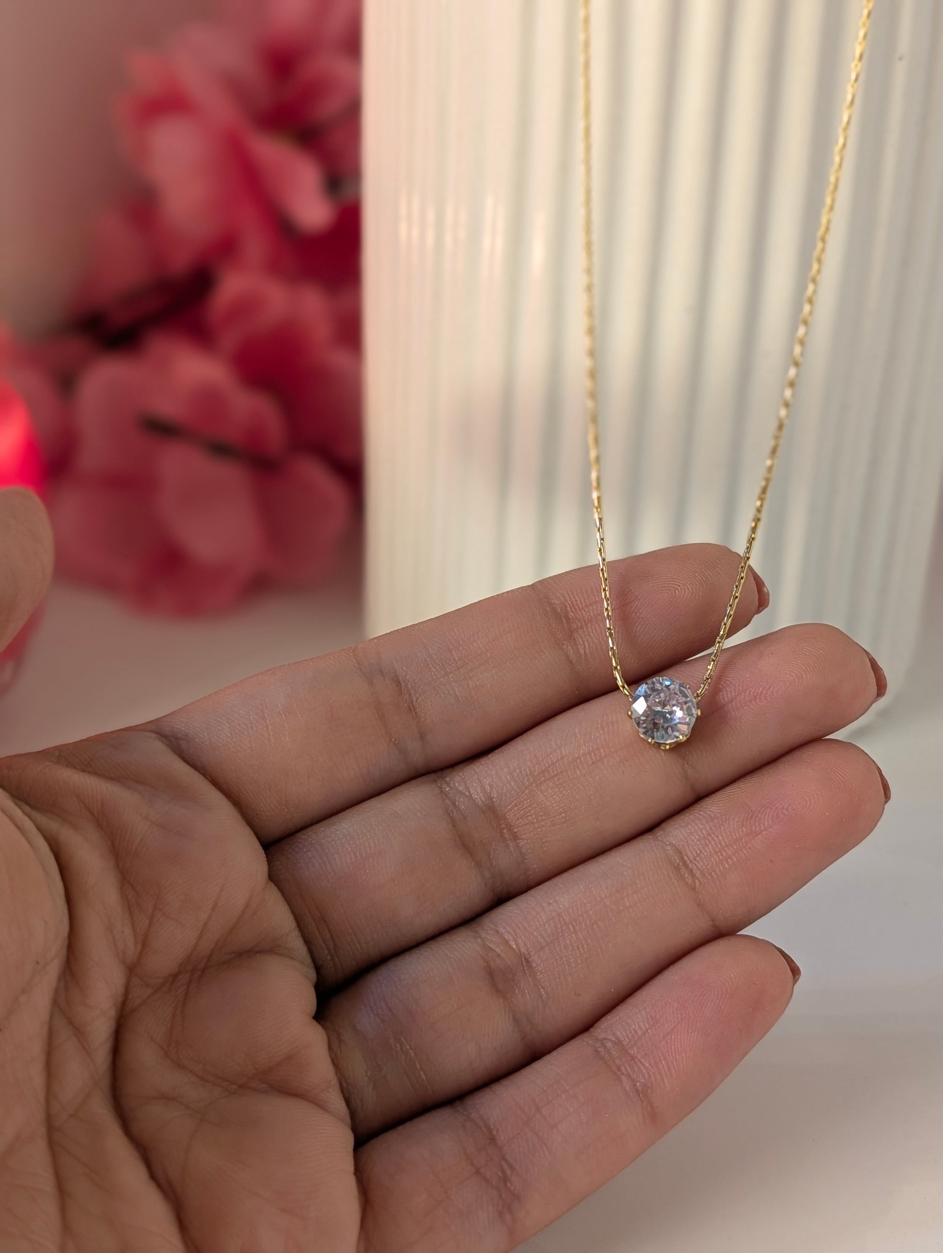 Gold necklace with a diamond pendant held between fingers against a blurred background