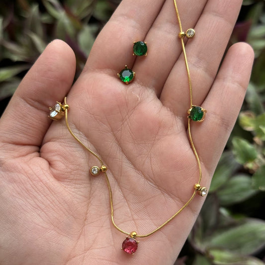 Gold bracelet with green and red gemstones on a hand against a blurred plant background
