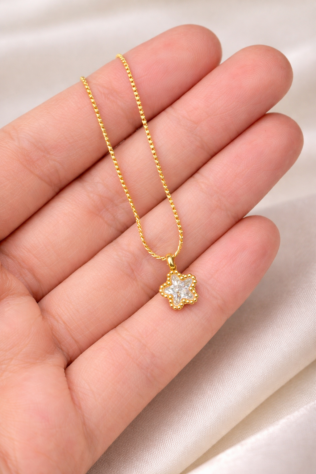 Gold necklace with a star-shaped pendant held between fingers on a light background