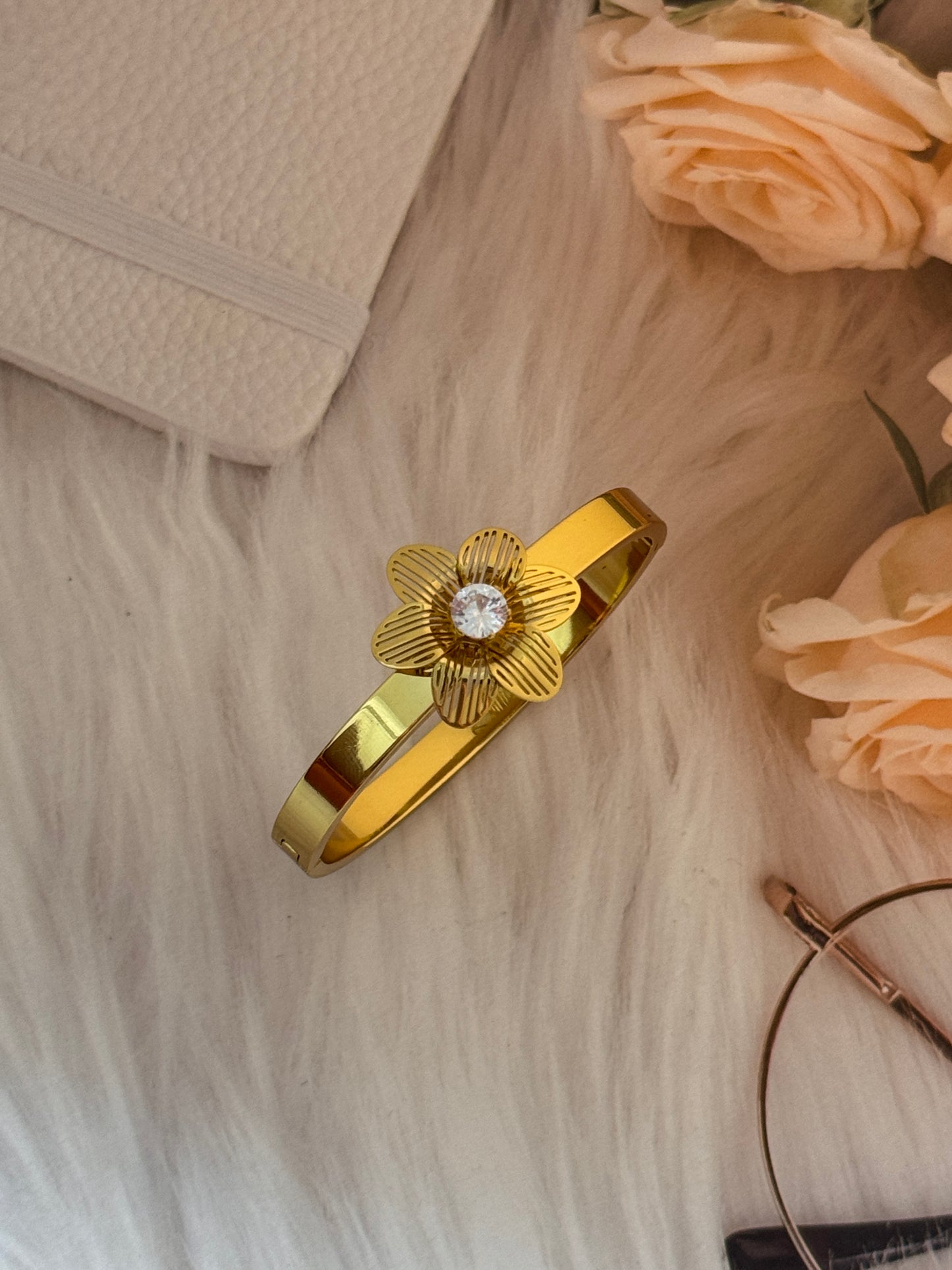 Gold hair clip with floral design on a textured surface with flowers and a book.