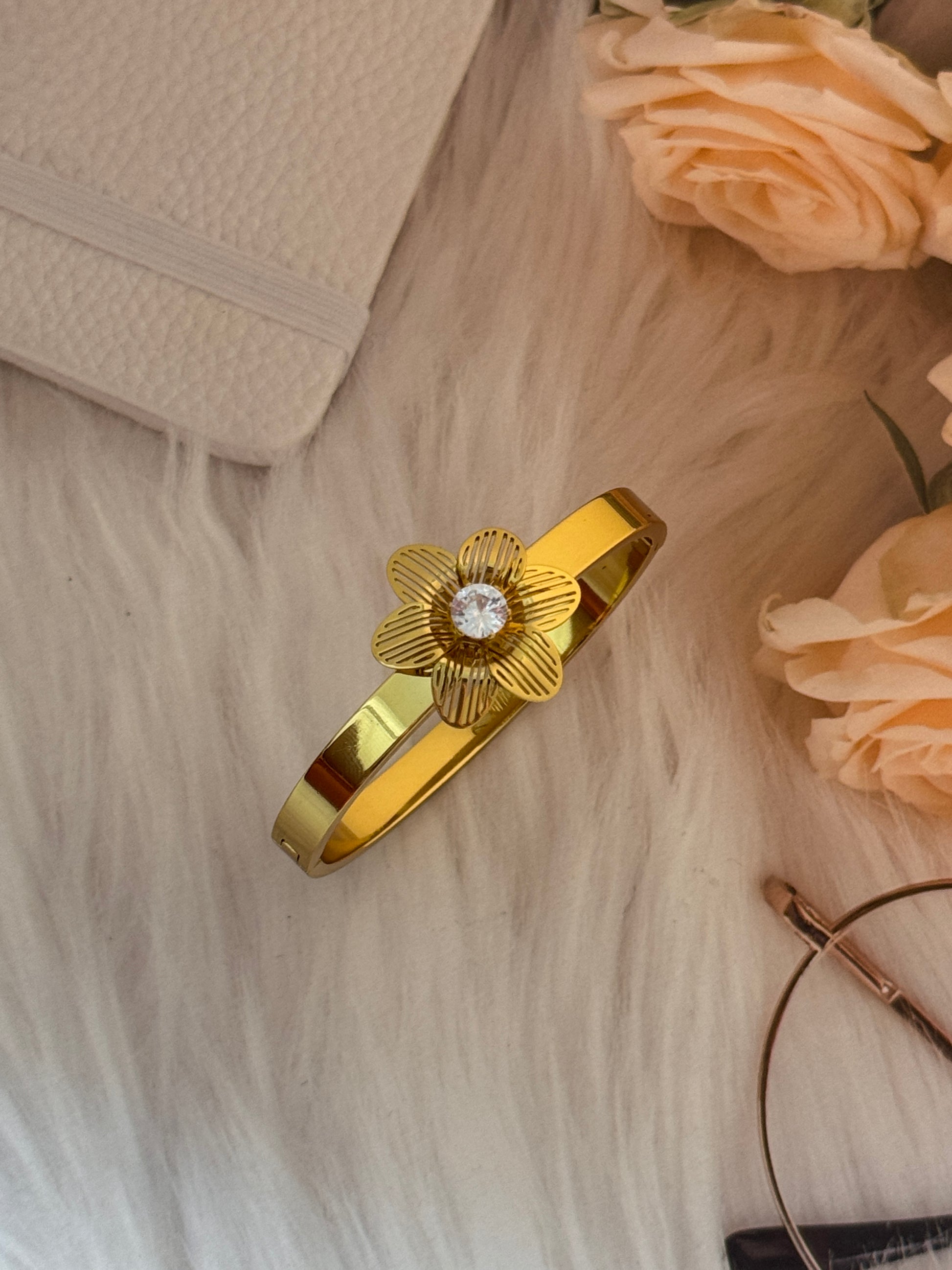 Gold hair clip with floral design on a textured surface with flowers and a book.