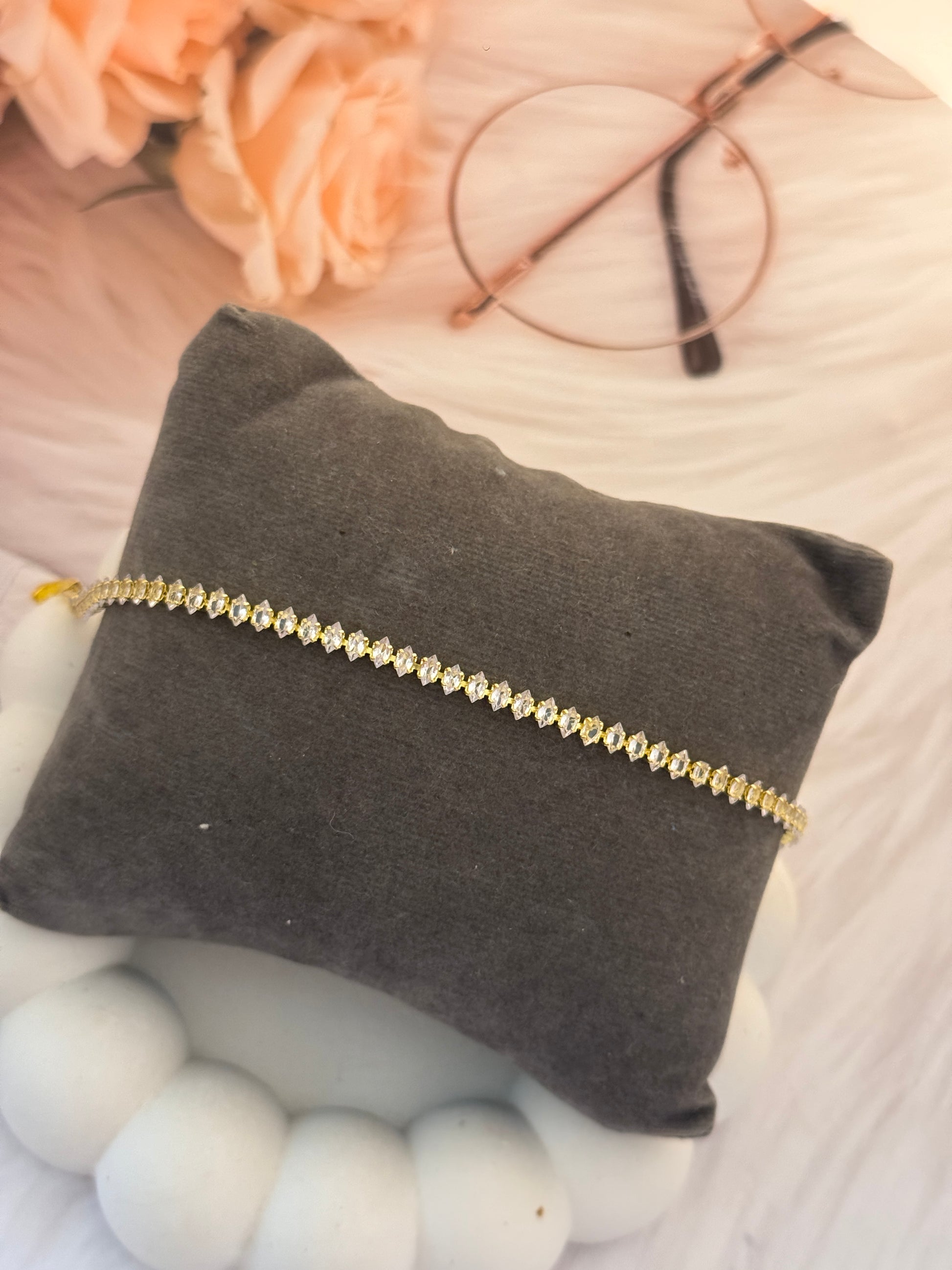 Gold bracelet on a gray pillow with flowers and glasses in the background