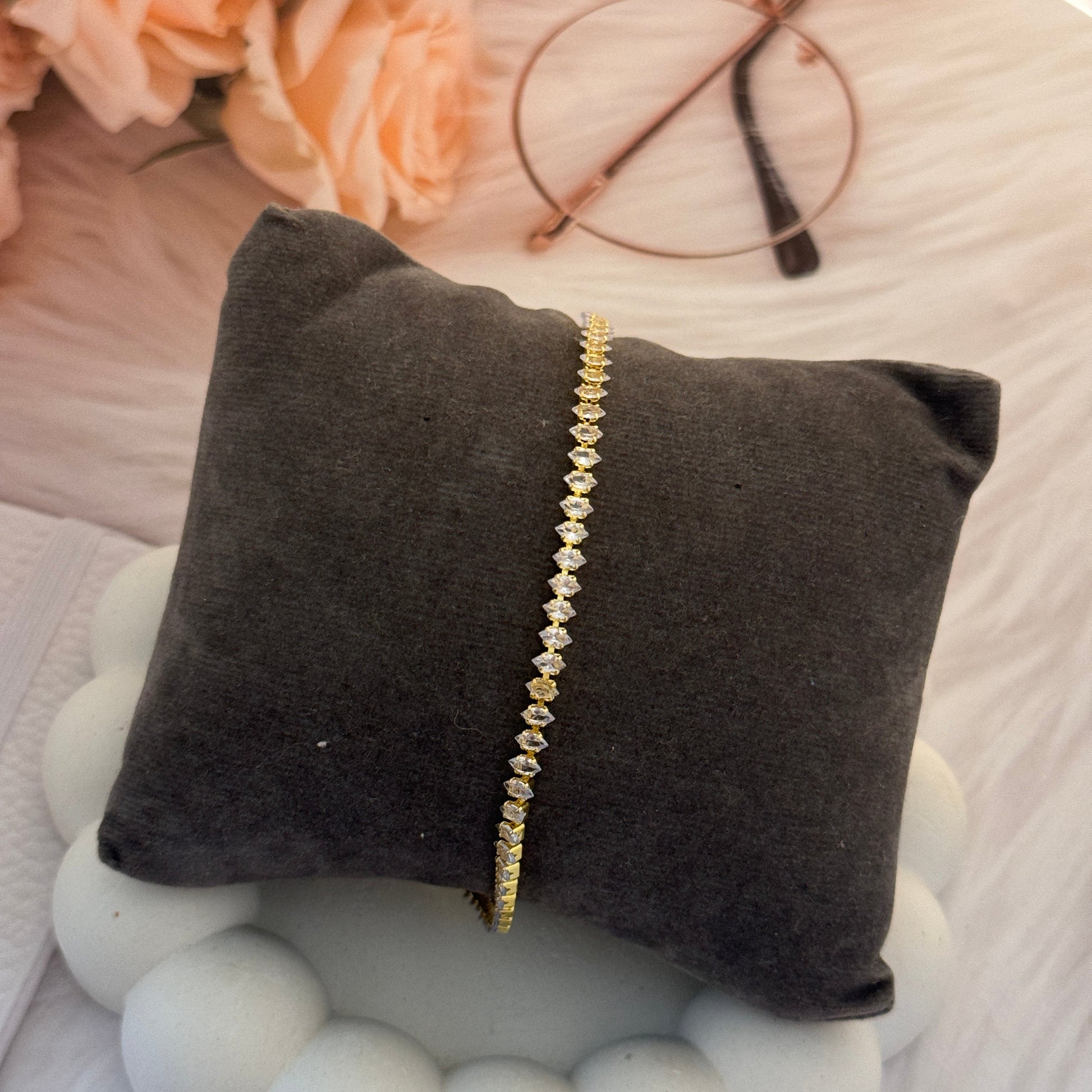 Gold bracelet on a gray pillow with flowers and beads in the background