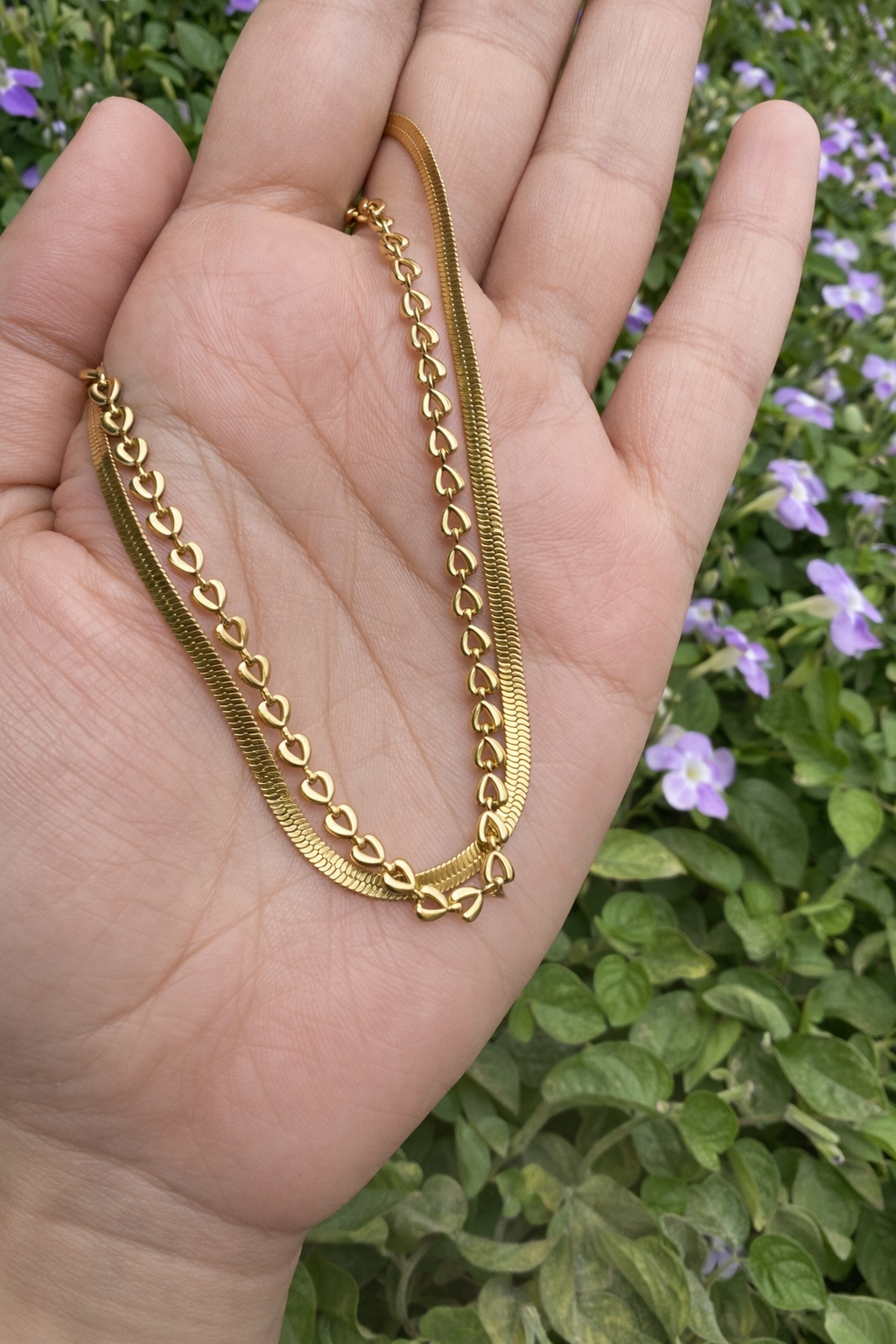 Gold chain held in a hand with a blurred green and purple plant background