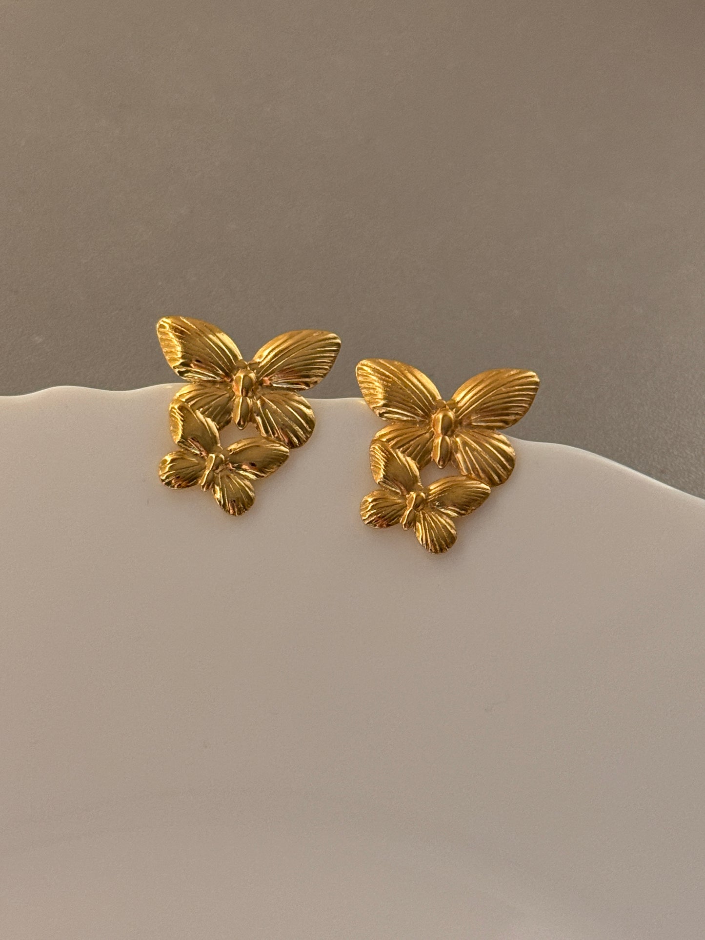 Gold butterfly earrings on a neutral background