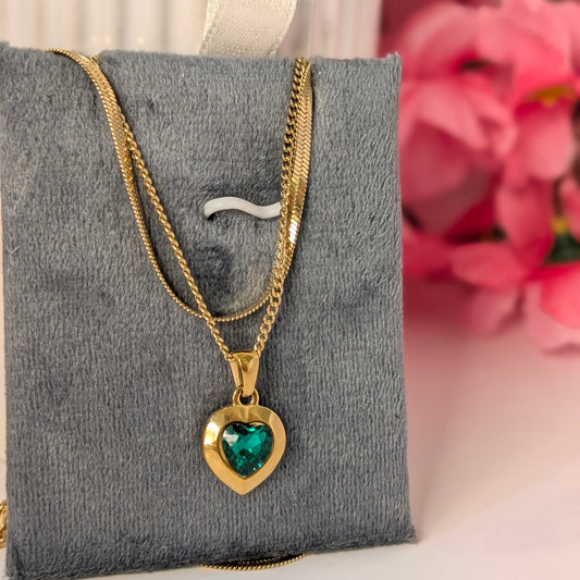 Gold necklace with a heart-shaped green gemstone pendant on a gray jewelry display box.