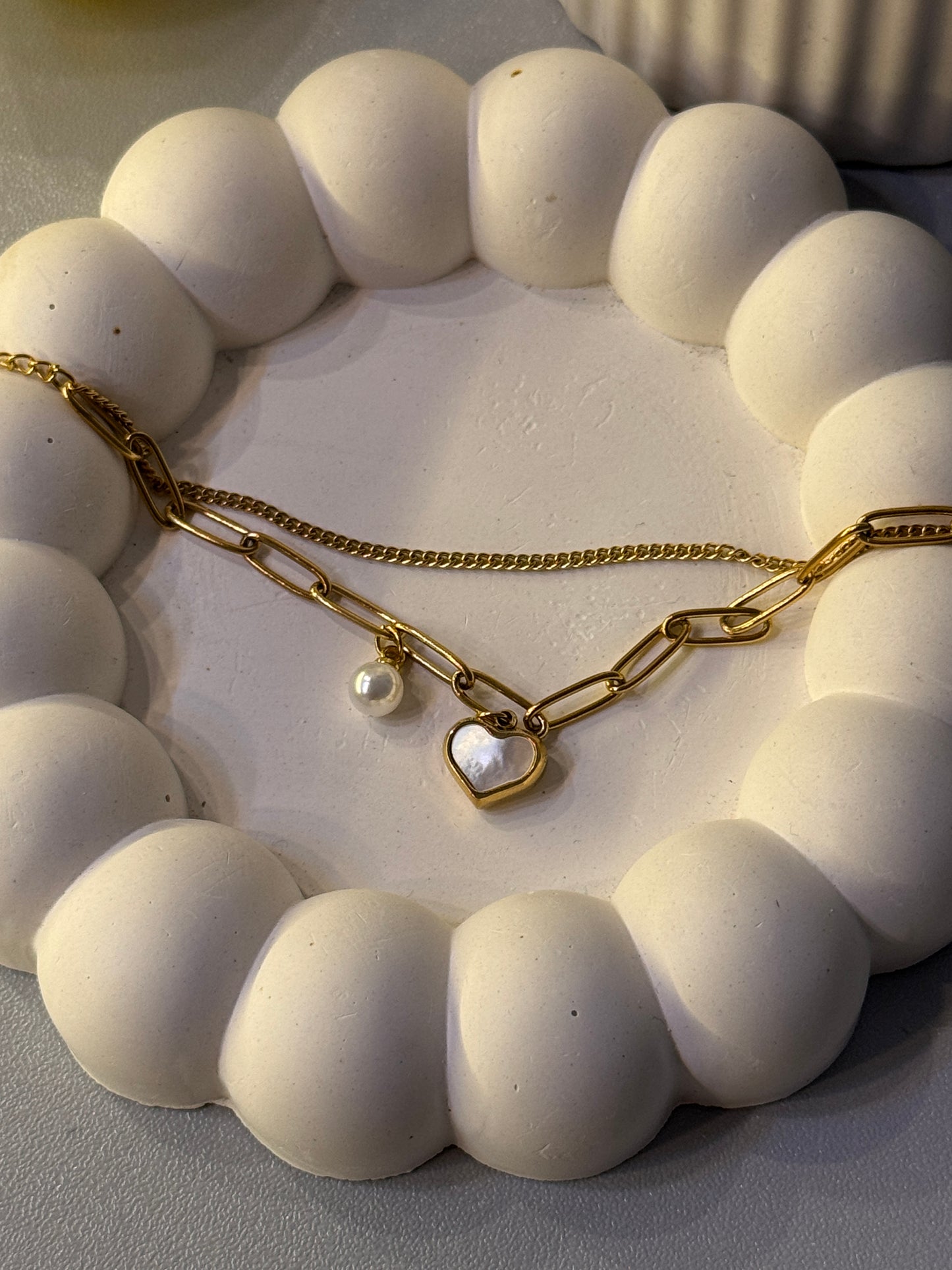 Gold chain necklace with a heart pendant on a white stone surface