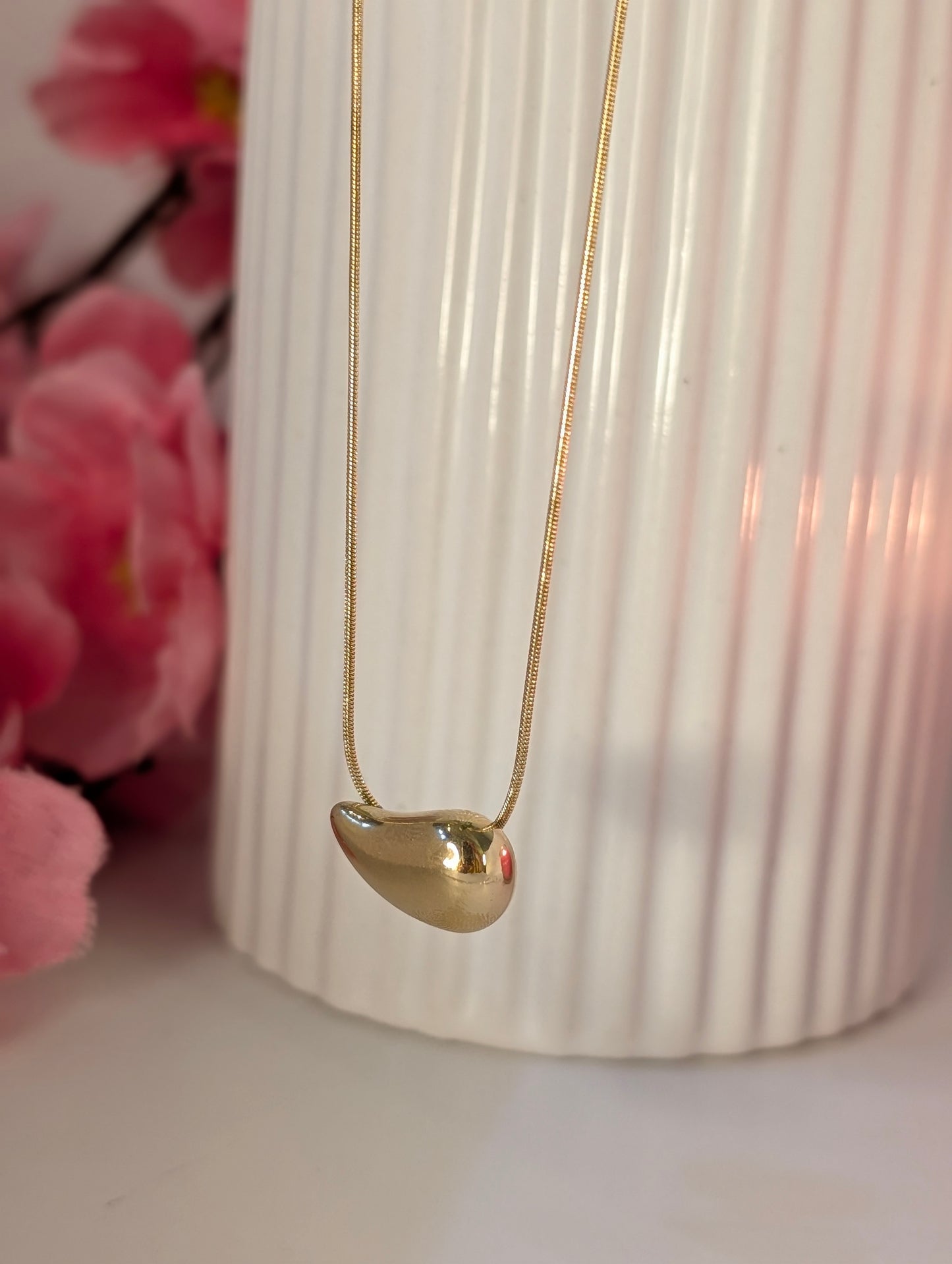 Gold necklace with a pendant in front of a white vase and pink flowers