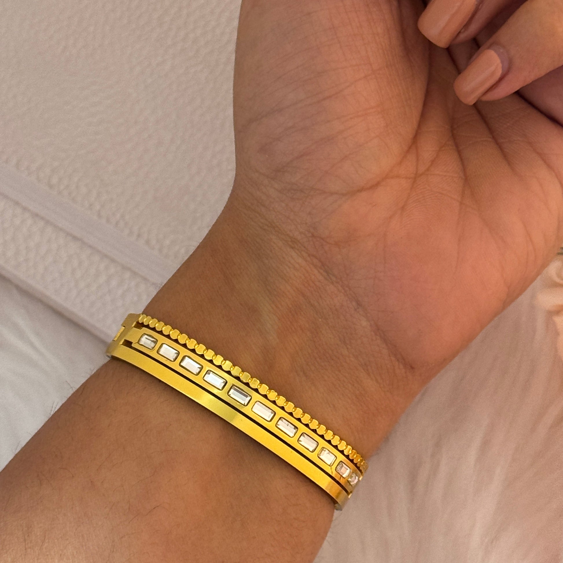 Gold bracelet on a wrist with a neutral background