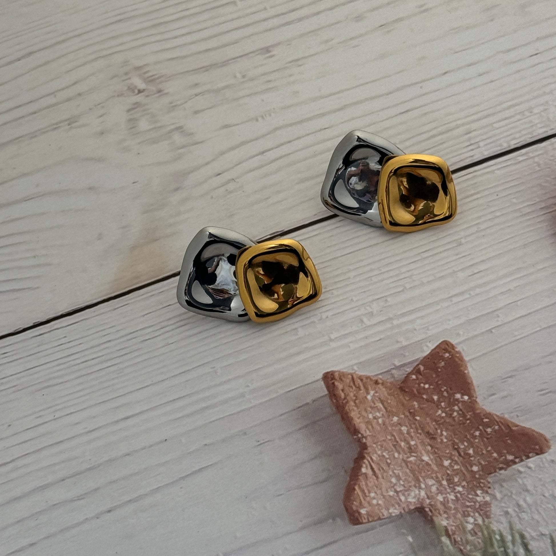 Pair of gold and silver square-shaped earrings on a light wooden surface.