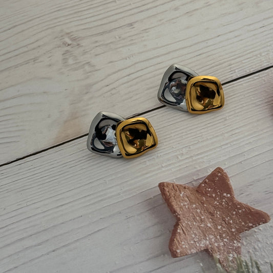 Pair of gold and silver square-shaped earrings on a light wooden surface.