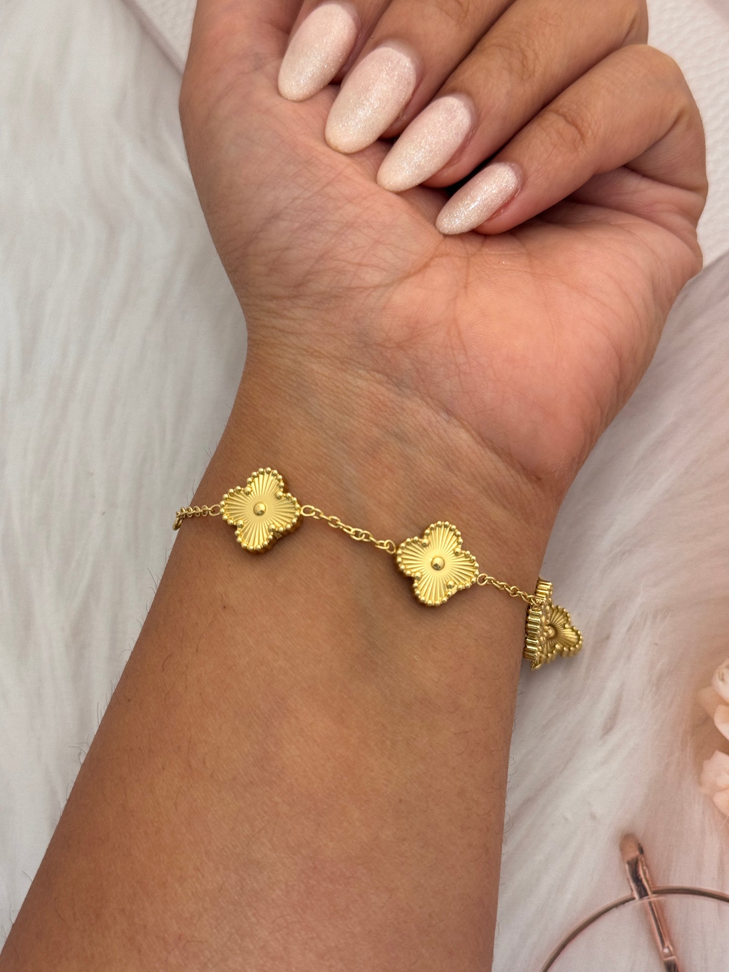 Gold bracelet with floral designs on a wrist against a neutral background