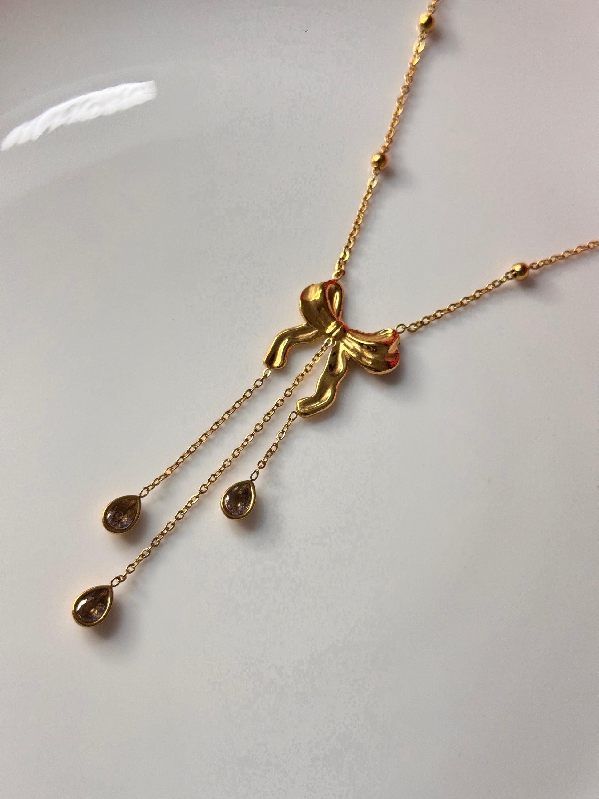 Gold necklace with a bow and droplets on a white background