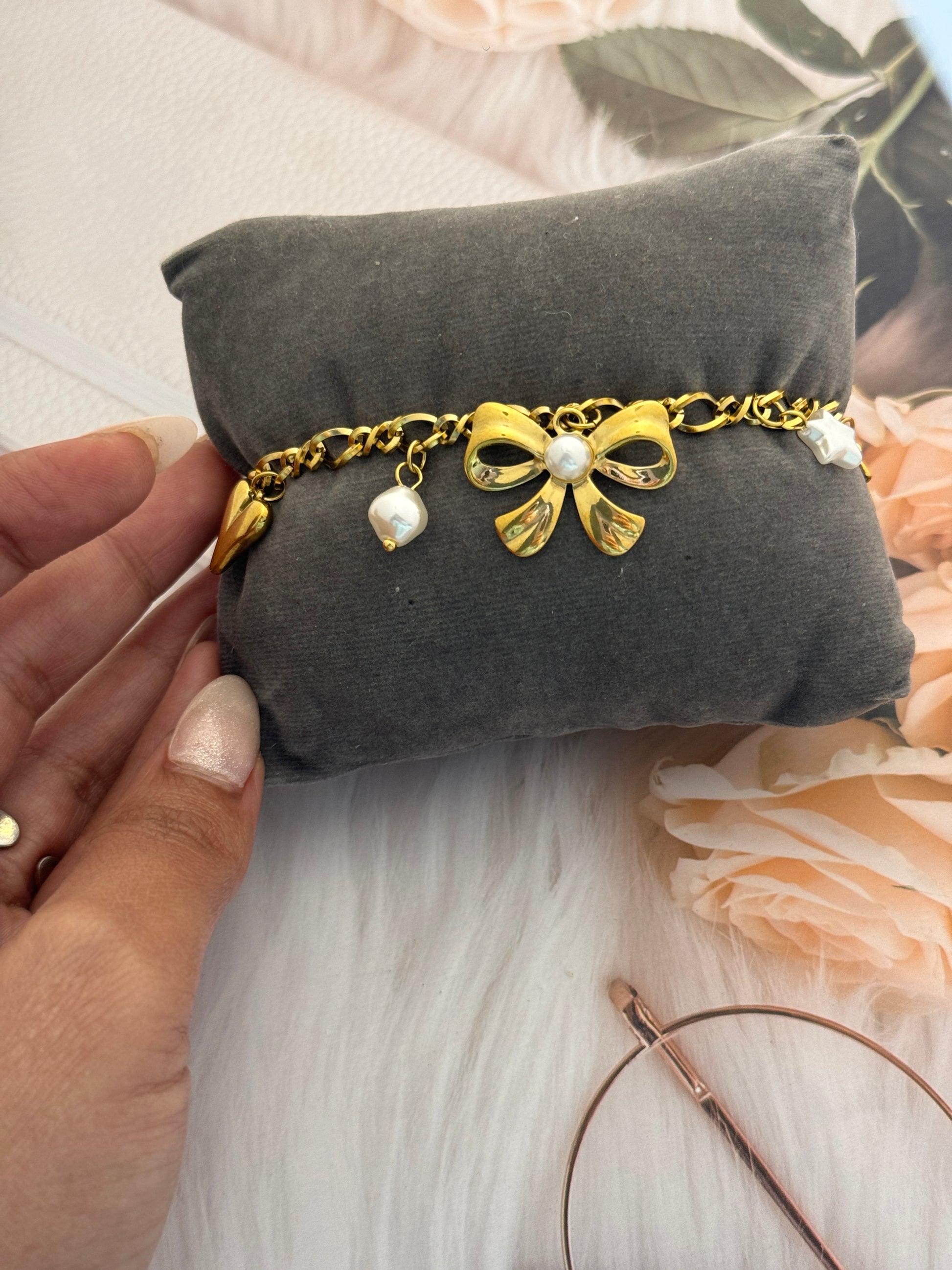 Gold bracelet with bow and pearl details on a gray pillow