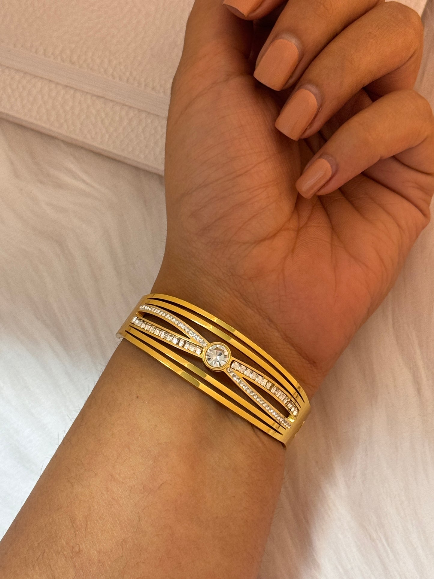 Gold bracelet with a diamond on a wrist against a neutral background