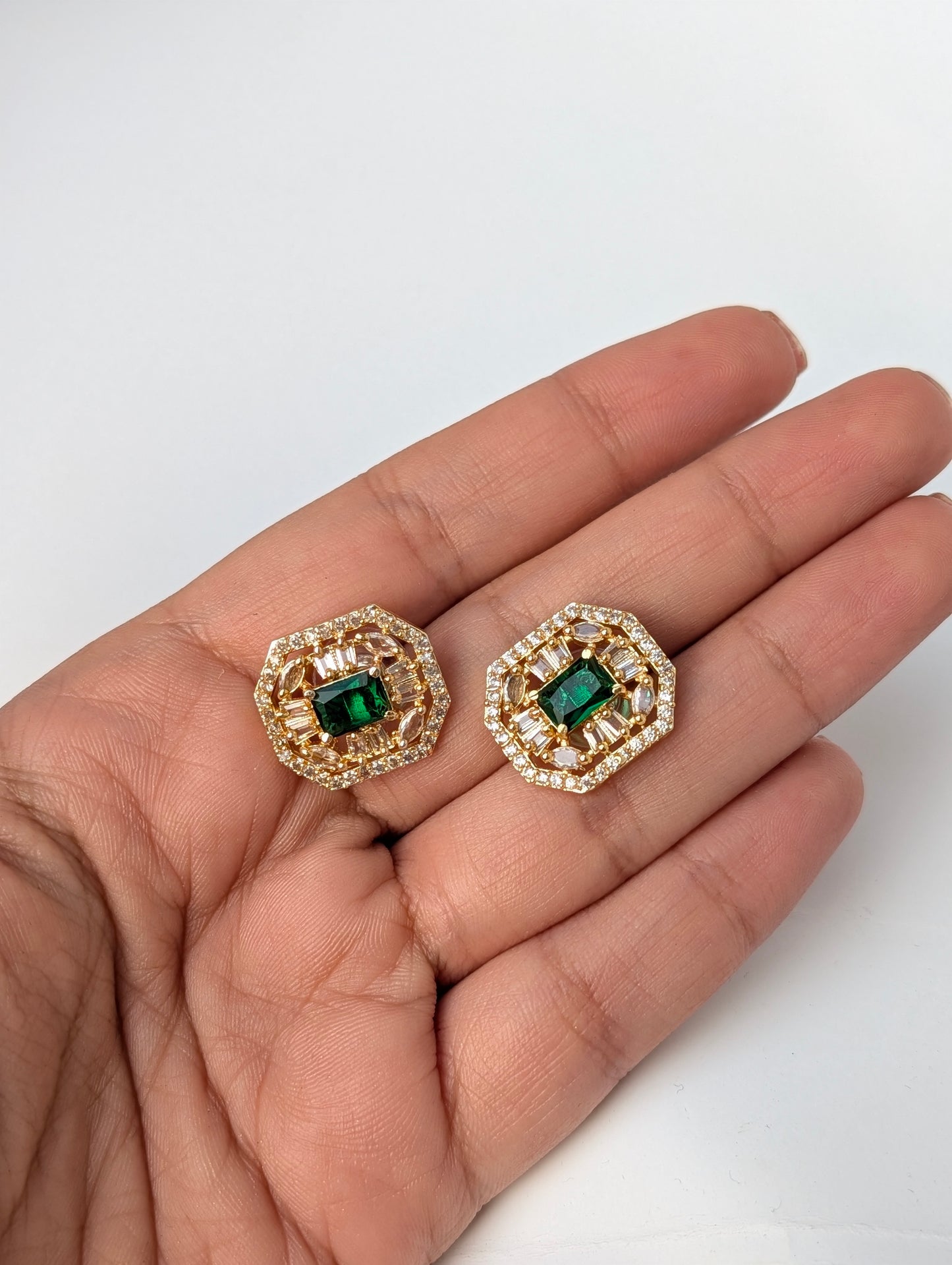 Gold earrings with green gemstones held in a hand on a white background