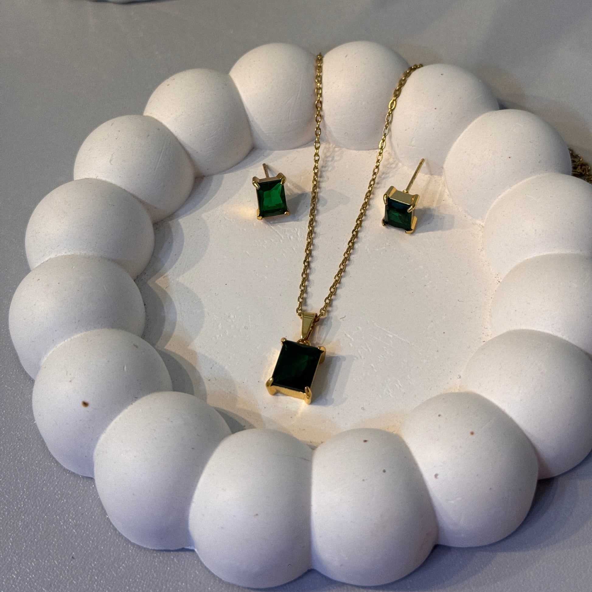 Gold chain with green gemstone earrings on a white stone surface