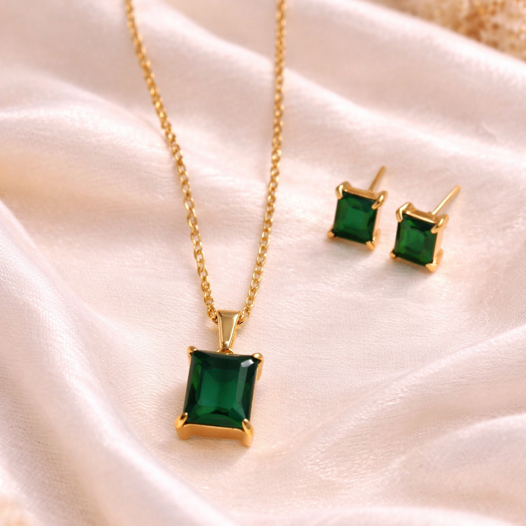 Gold necklace and earrings with green gemstones on a soft fabric background