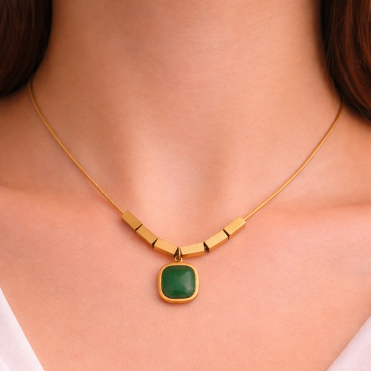 Gold necklace with a green pendant on a person wearing a white top.