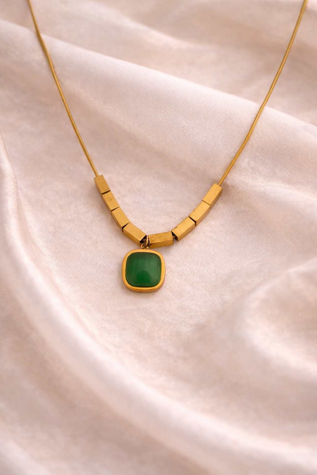 Gold necklace with a green pendant on a beige fabric background