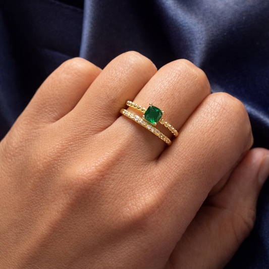 Gold ring with a green gemstone on a hand against a dark blue fabric background