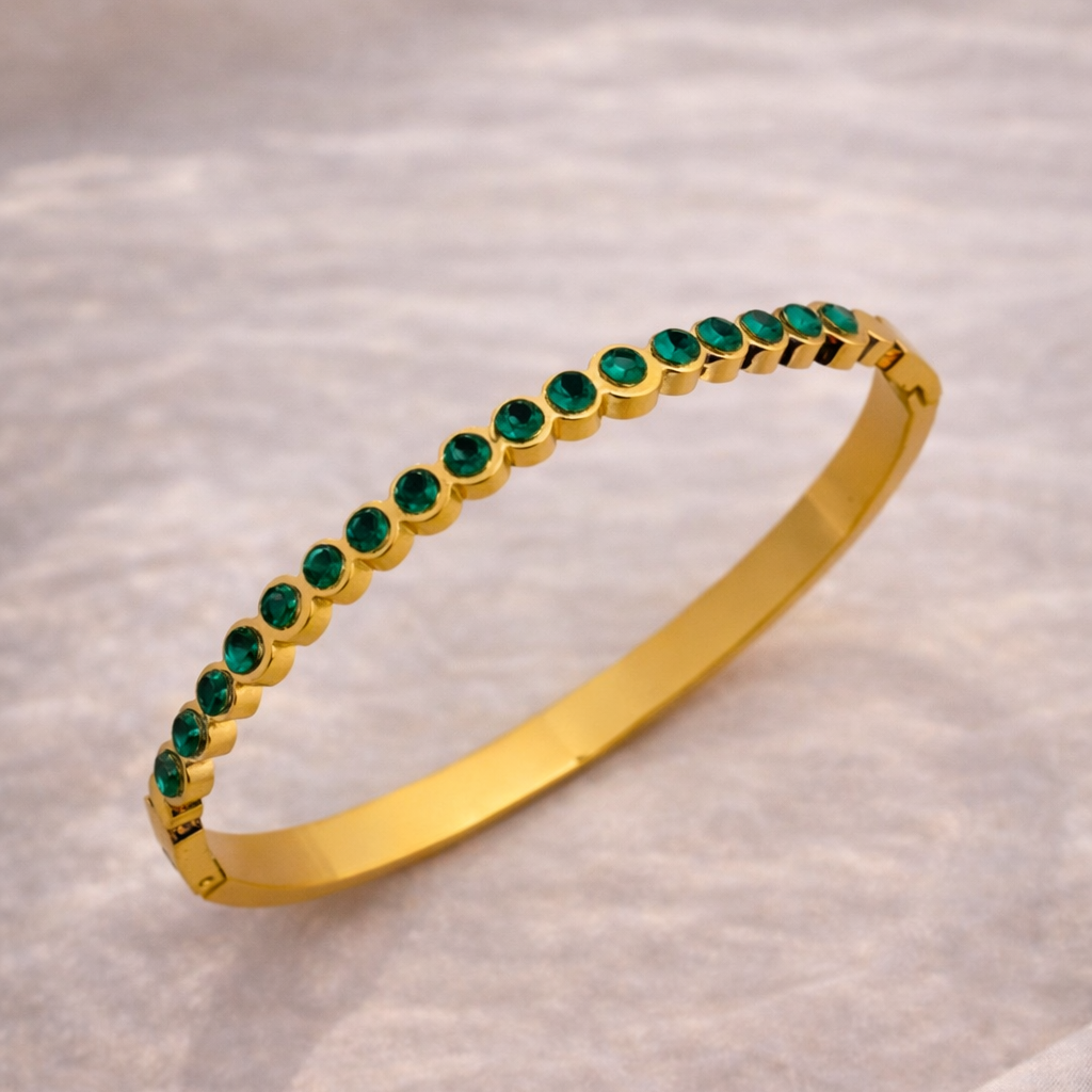 Gold bracelet with green gemstones on a light fabric background