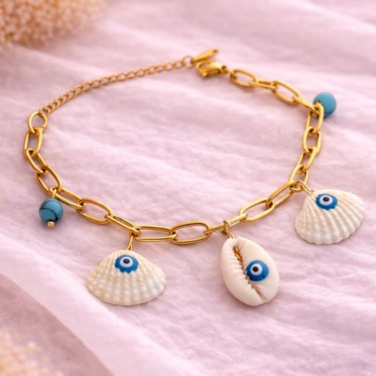 Gold bracelet with shell charms featuring eye designs on a soft pink fabric background