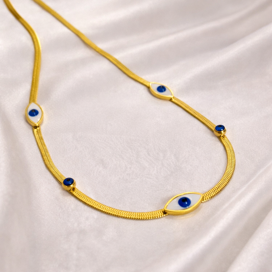 Gold necklace with blue eye-shaped stones on a white fabric background