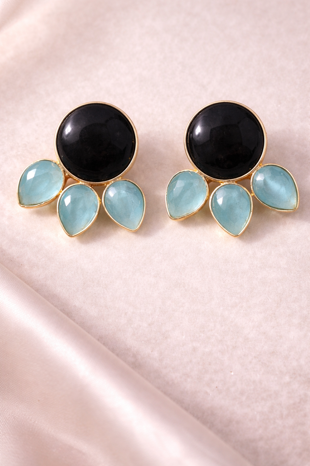 Pair of earrings with black and light blue stones on a pink fabric background