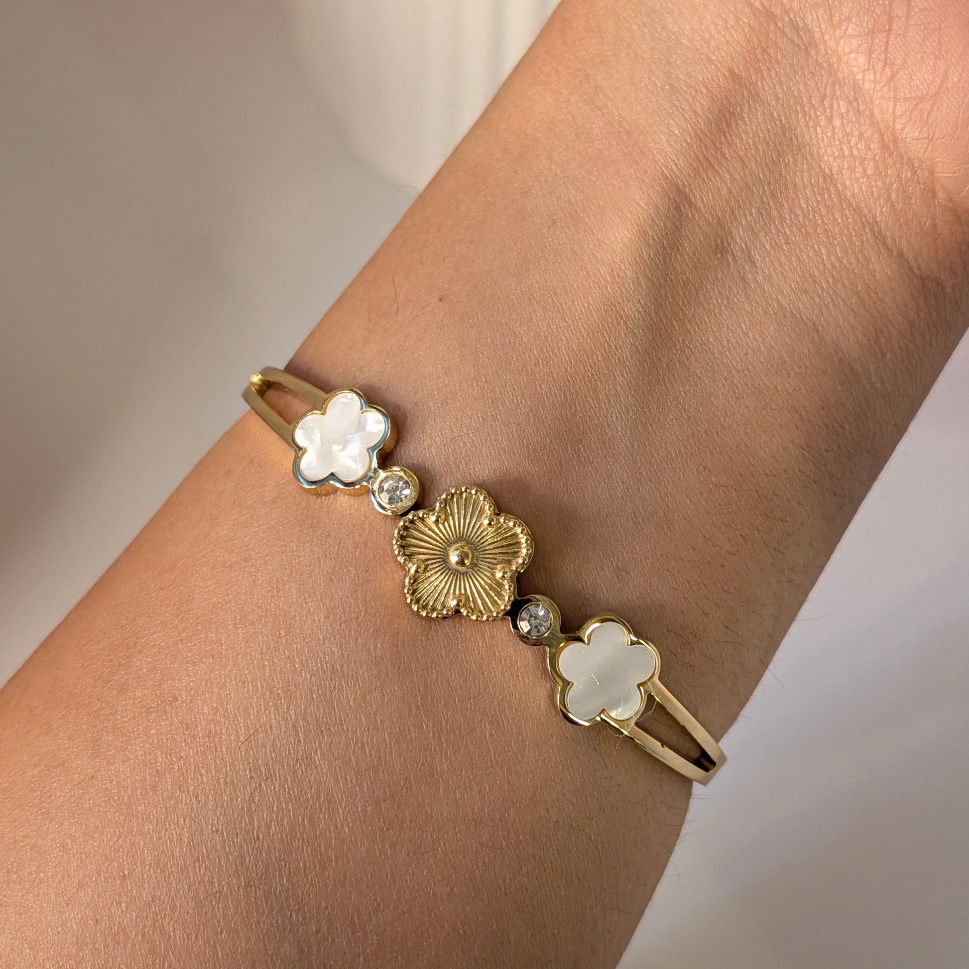 Gold bracelet with floral designs on a wrist against a neutral background