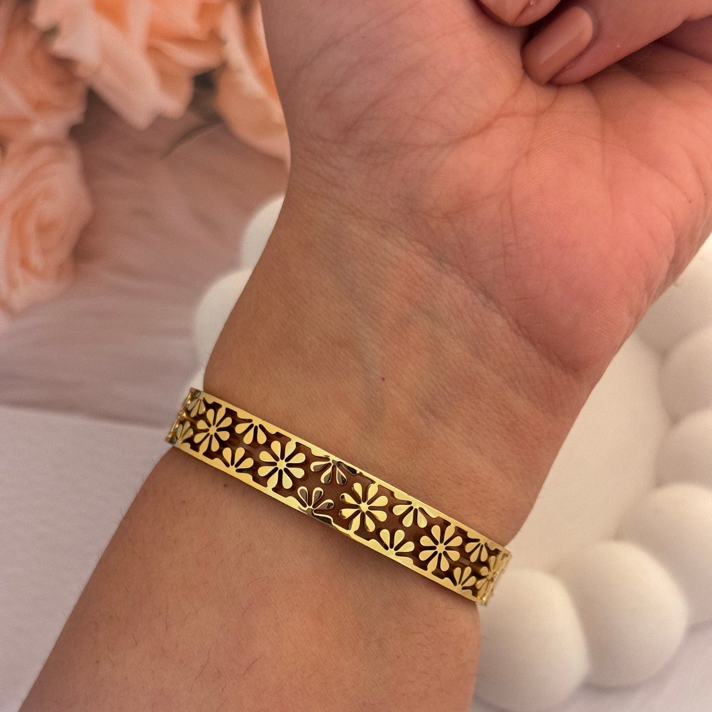 Gold bracelet with intricate design on a wrist, blurred background