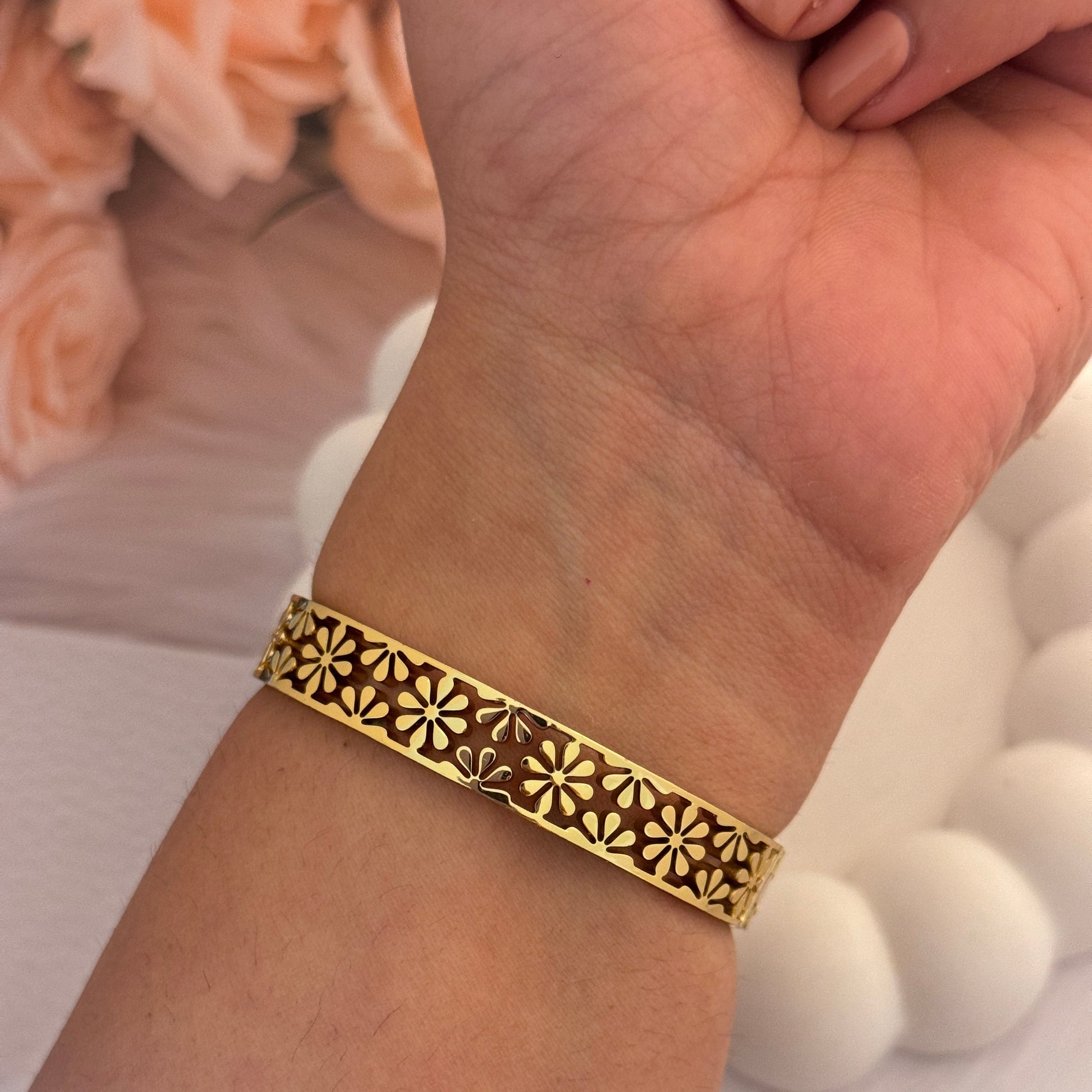 Gold bracelet with intricate design on a wrist, blurred background