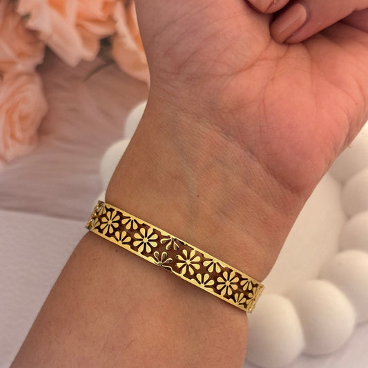 Gold bracelet with intricate design on a wrist, blurred background